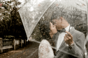 Bride and groom kissing under a clear umbrella on a rainy day - EventLavs.com
