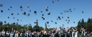 Graduating students in caps and gowns celebrating outdoors by tossing their graduation caps into the air under a clear blue sky.