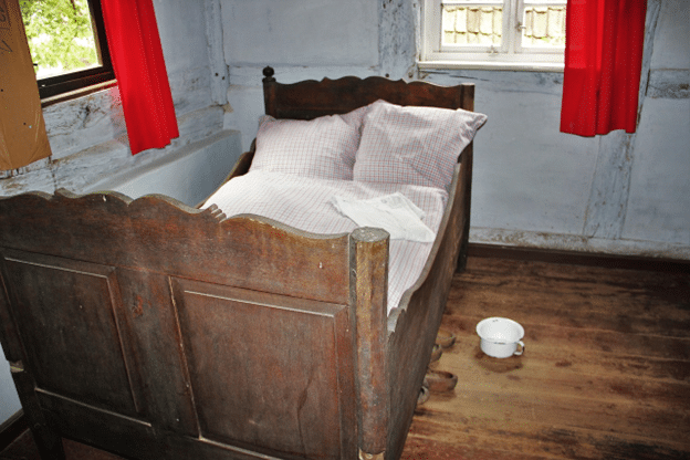 Historic wooden bed with a chamber pot on the floor.