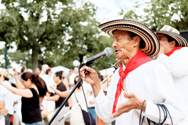 Elder man in traditional sombrero singing into a microphone at a Hispanic Heritage Month festival.