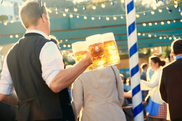 Server carrying multiple beer steins at an outdoor brewery festival.