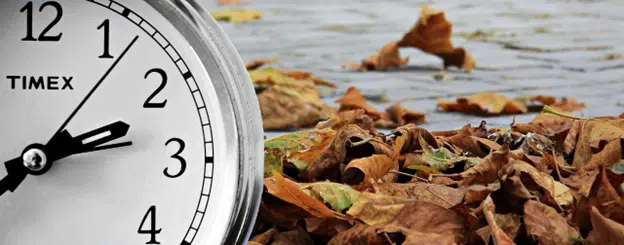 Time for Fall events is closer that you think. Close-up clock beside fallen autumn leaves on wet pavement.
