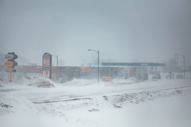Snow-covered commercial area during a winter storm with low visibility.