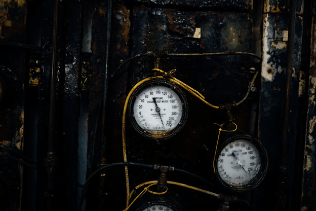 Close-up of pressure gauges on worn industrial pipes in a dark mechanical room.