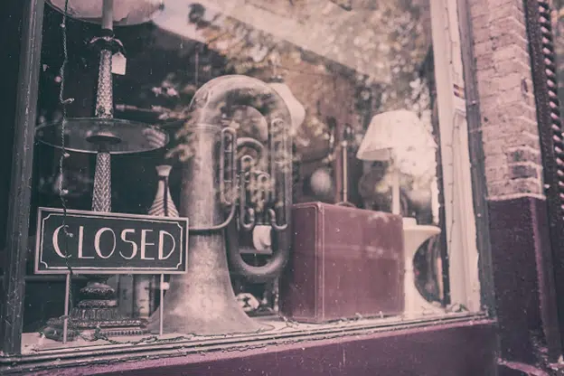 Storefront window with a closed sign displayed beside vintage items on a shelf.