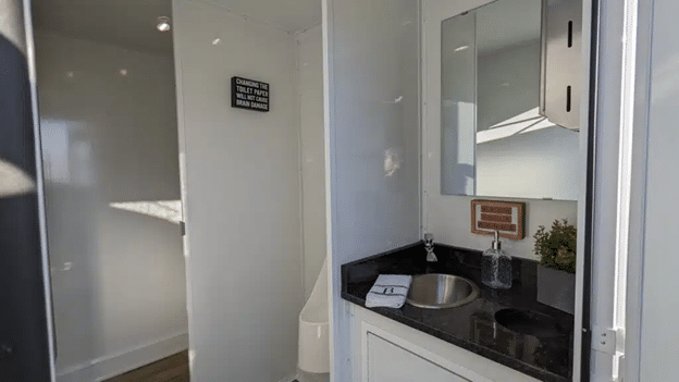 Interior of a luxury restroom trailer with sink, mirror, and modern amenities.