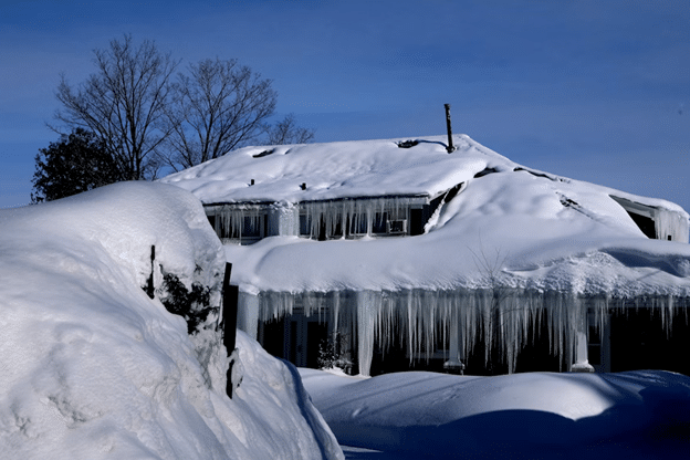 House covered in deep snow with large icicles hanging from the roofline.