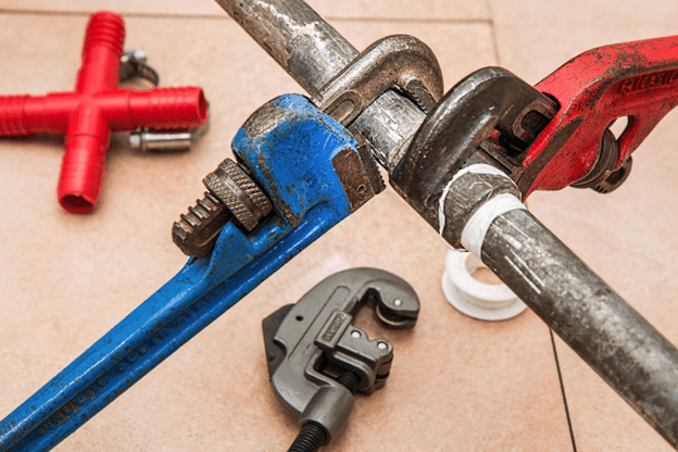 Plumbing tools gripping a damaged metal pipe during a repair job.