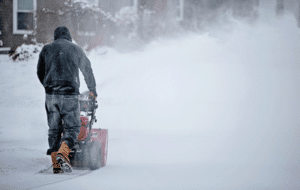 Man using a snowblower during heavy snowfall in winter conditions.
