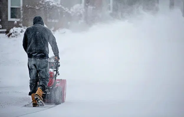 Man using a snowblower during heavy snowfall in winter conditions.